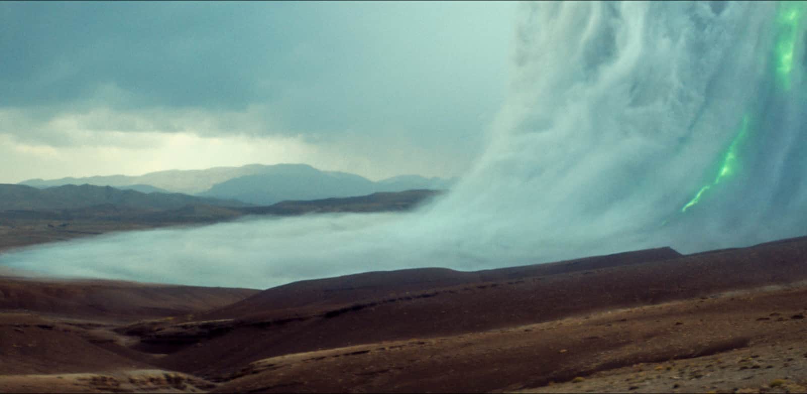 Paysage désertique avec un lac brumeux, des montagnes au loin et une aurore boréale verdoyante.