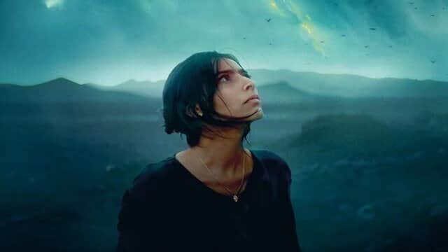 Une femme regardant le ciel dans un paysage montagneux sombre.