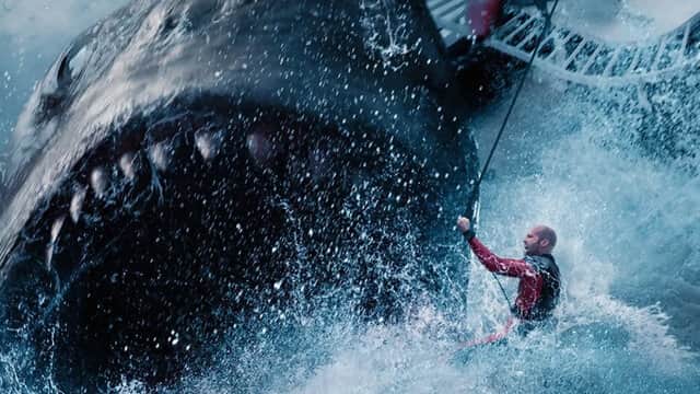 Un homme en combinaison rouge face à un énorme requin dans une mer agitée.
