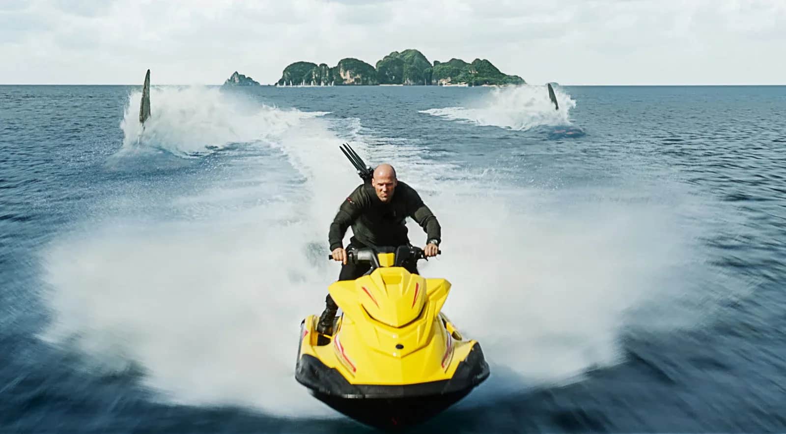 Un homme chauve sur un scooter des mers jaune, fonçant sur l’océan vers une île, poursuivi par des requins.