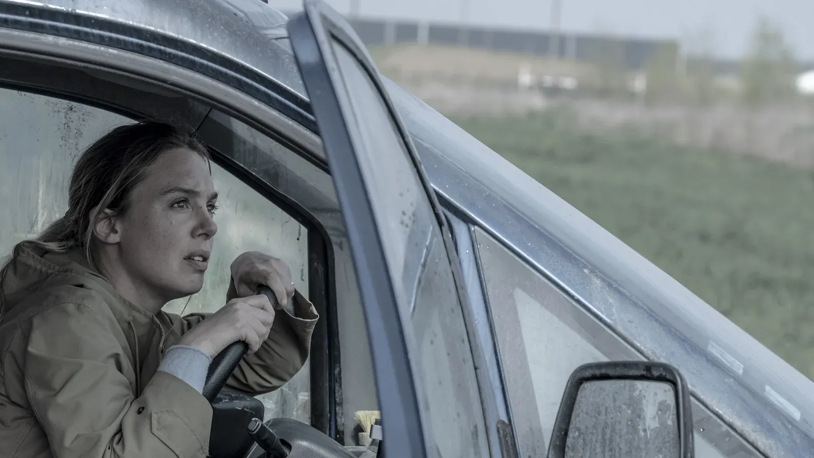 Une femme au volant d’une voiture, observant l’extérieur sous la pluie.