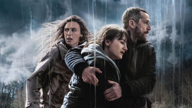 Trois personnes sous la pluie, un homme protégeant deux femmes, avec un ciel orageux en arrière-plan.