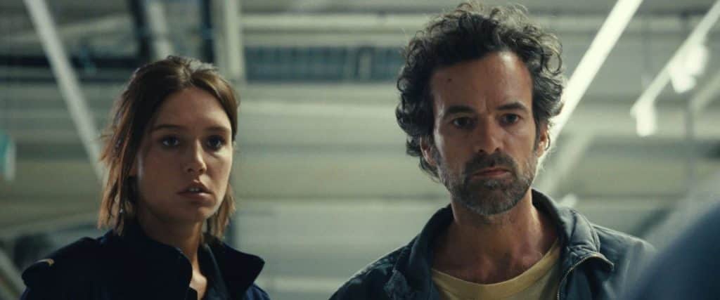 Deux personnes, une femme et un homme, regardent devant eux dans un bâtiment moderne.