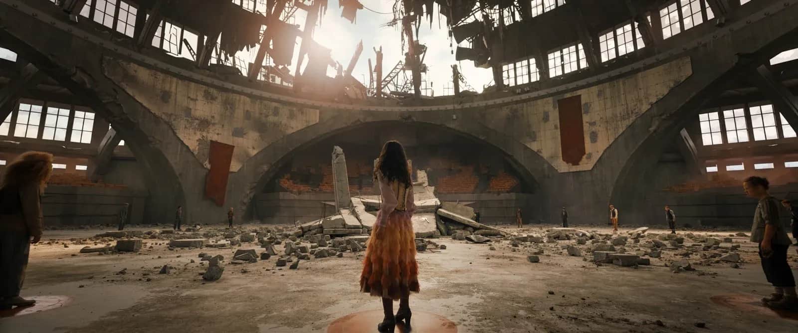 Une femme au centre d’un bâtiment industriel délabré, entourée de décombres et de plusieurs personnes