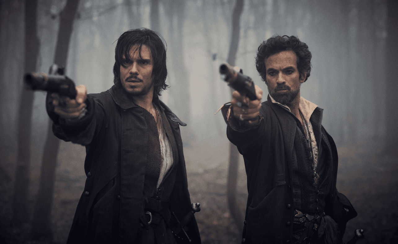 Deux hommes armés de pistolets se tiennent face caméra dans une forêt brumeuse.