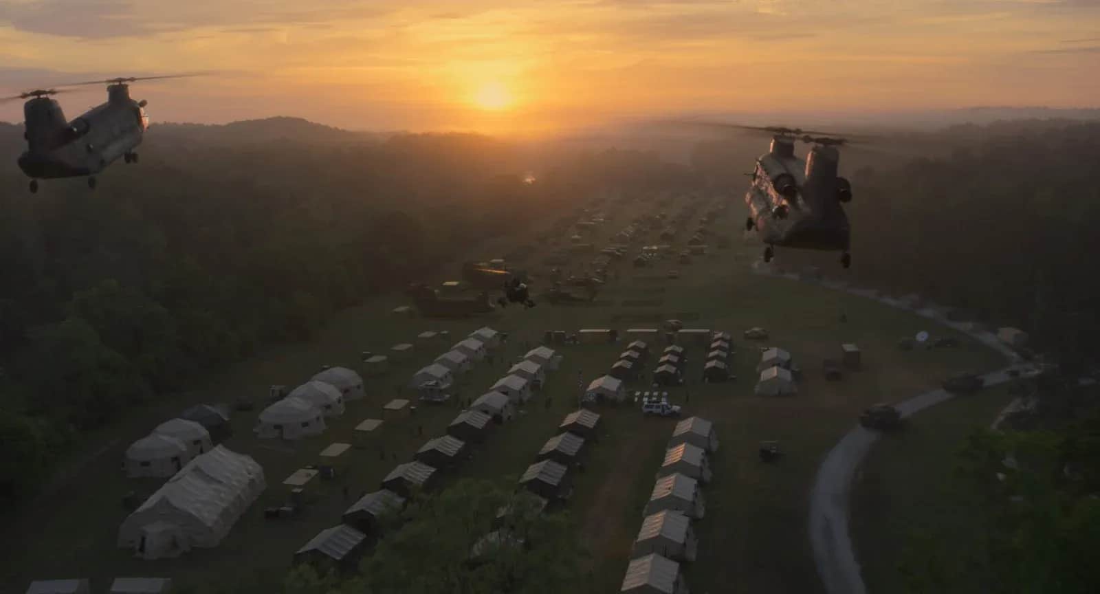 Deux hélicoptères survolent un camp de tentes au coucher du soleil.