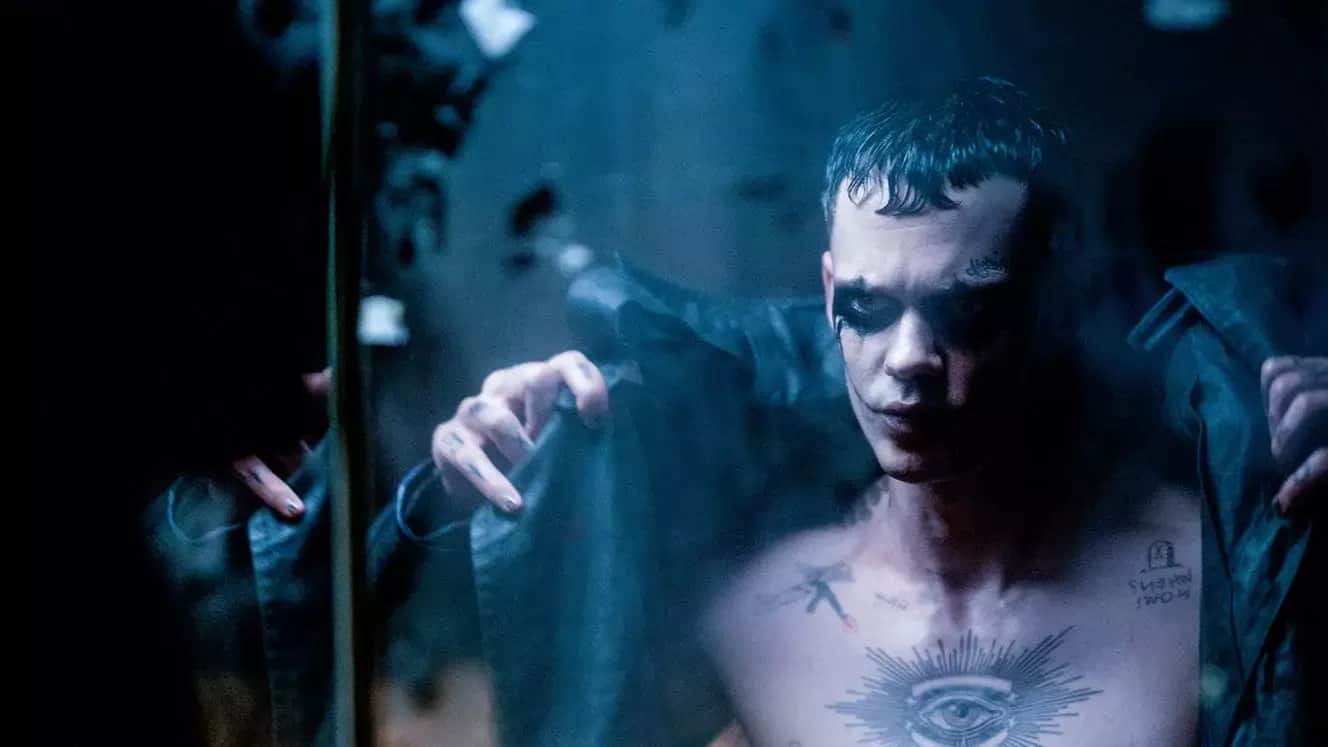 Un homme torse nu, tatoué, se regarde dans un miroir sous une lumière bleutée.