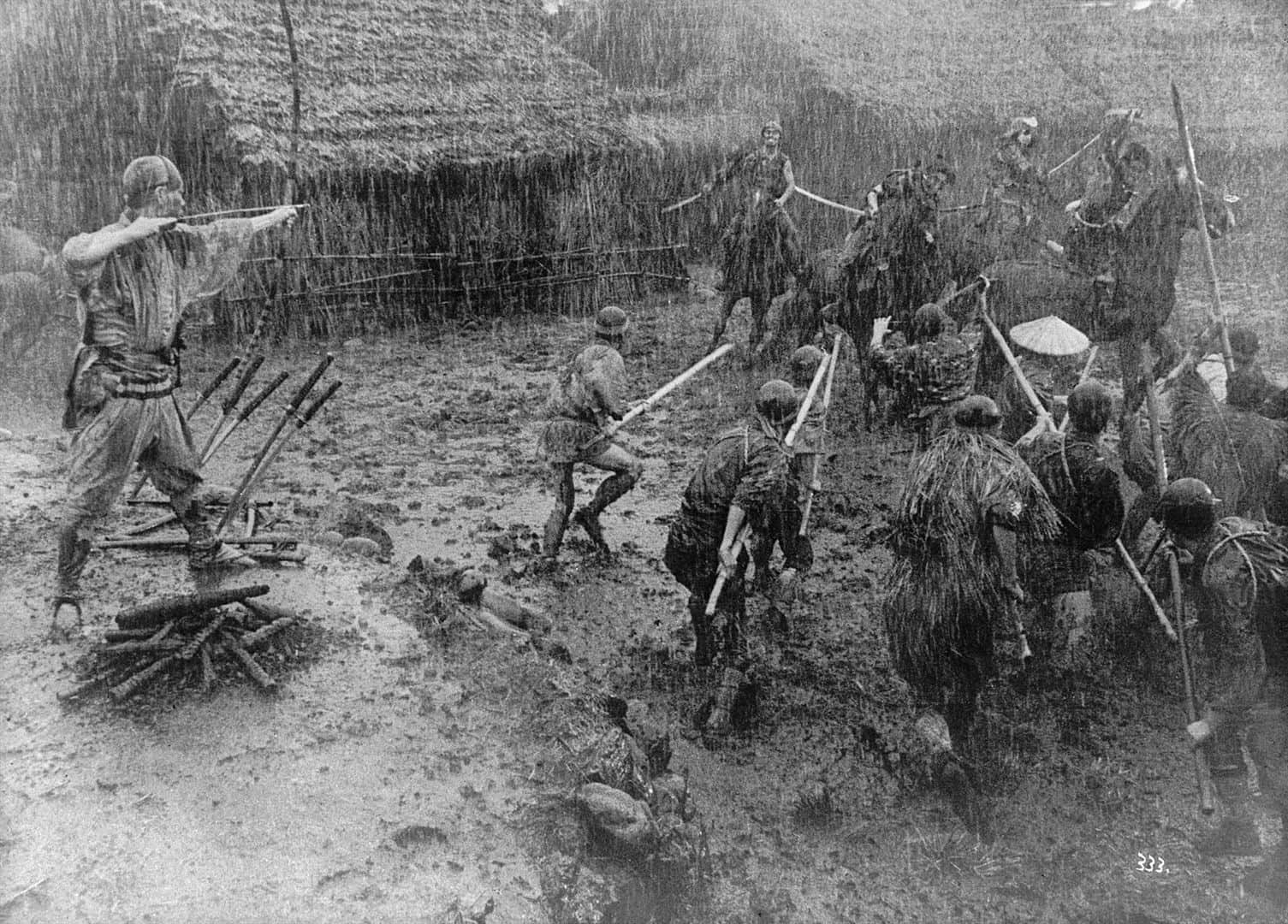 Un groupe de personnes armées, certaines portant des vêtements en feuillage, avancent sous la pluie dans la boue.