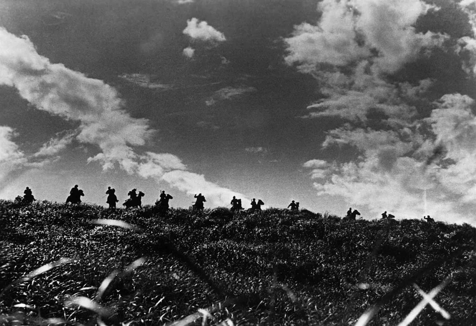 Un groupe de personnes avance sur une crête herbeuse sous un ciel nuageux en noir et blanc