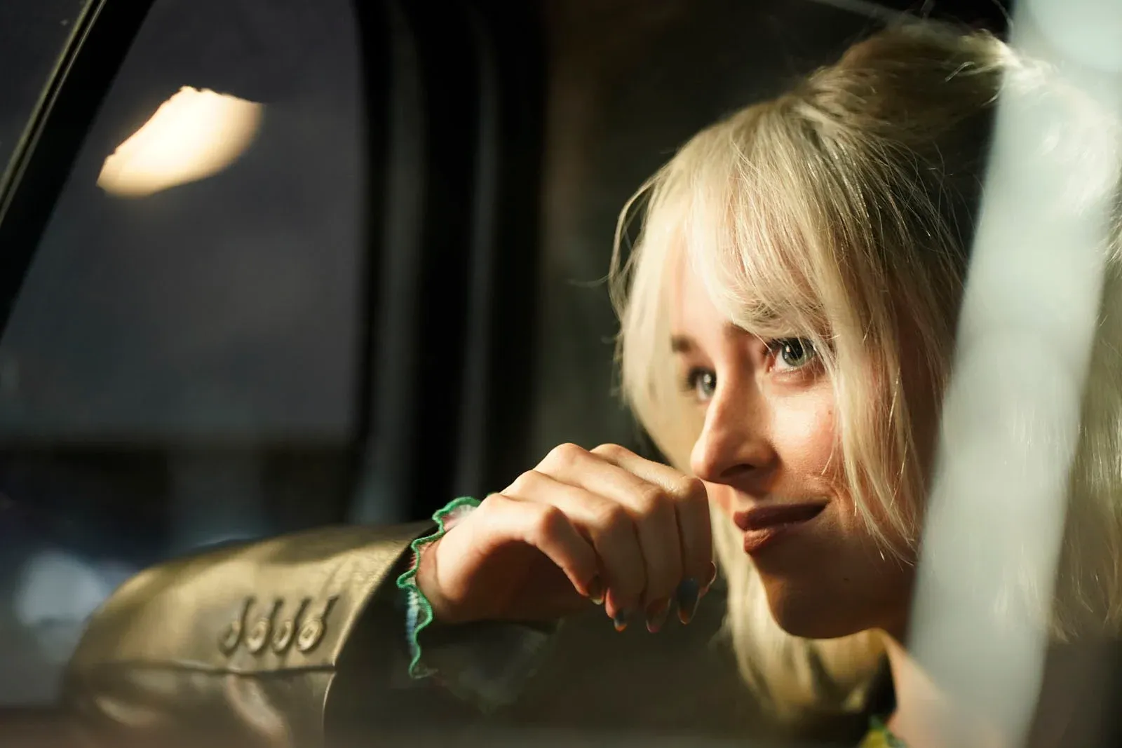 Femme blonde appuyée contre une vitre, le menton posé sur sa main.