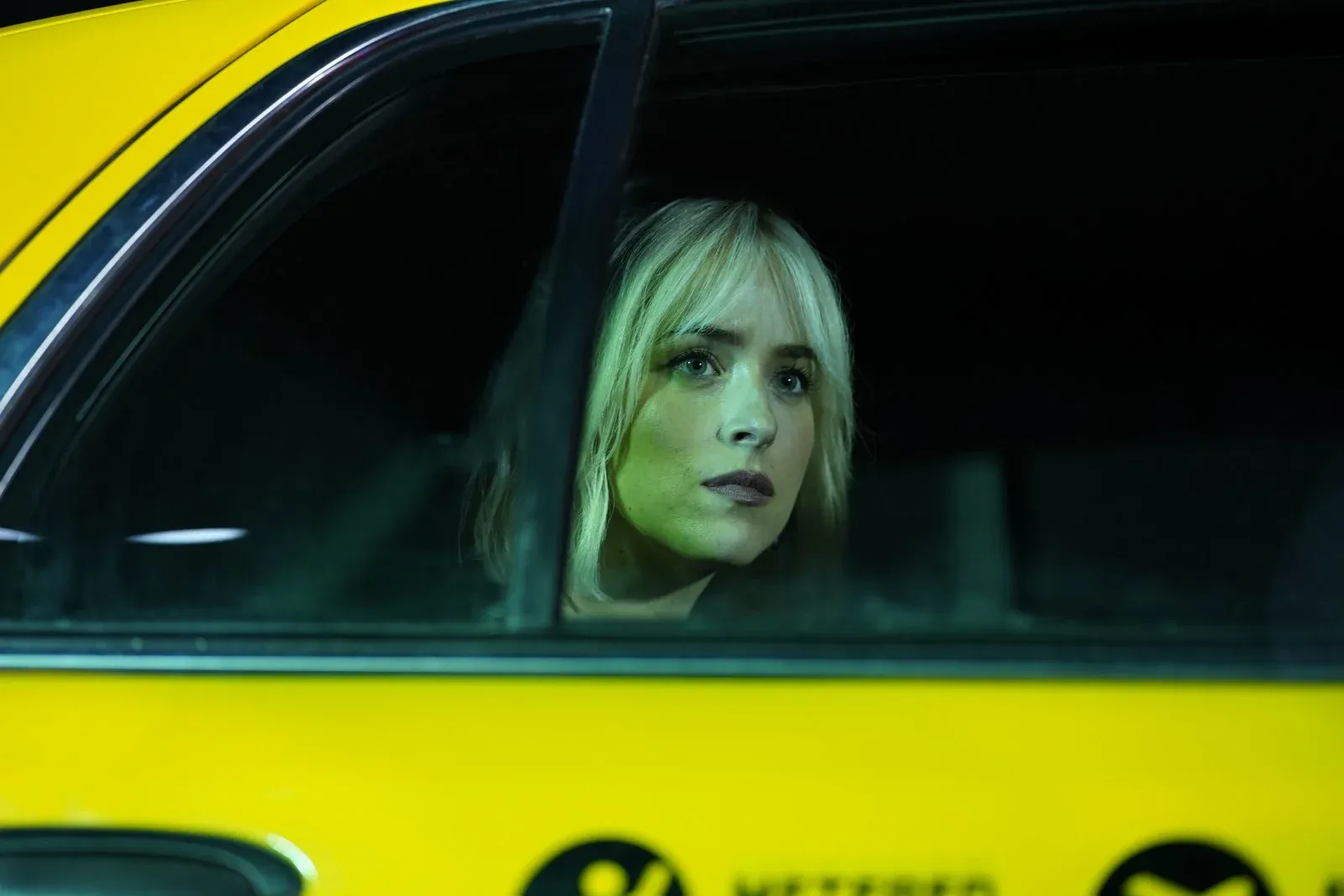 Femme blonde regardant par la fenêtre d’un taxi jaune dans l’obscurité