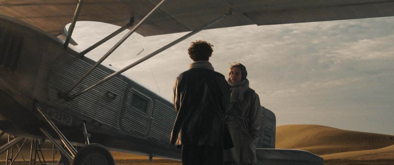 Deux personnes se tiennent devant un avion ancien, dans un paysage désertique.