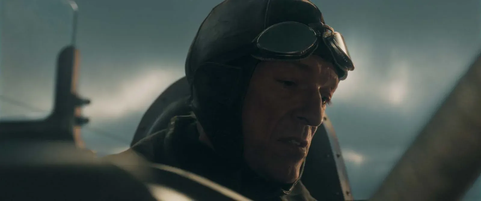 Homme portant un casque d’aviateur et des lunettes, assis dans le cockpit d’un avion.