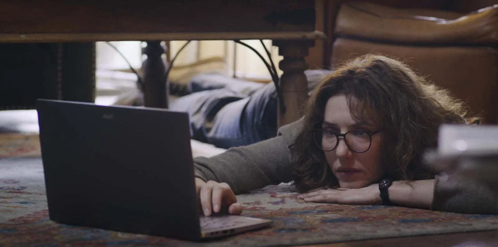 Femme portant des lunettes, allongée au sol devant un ordinateur portable, dans une chambre.