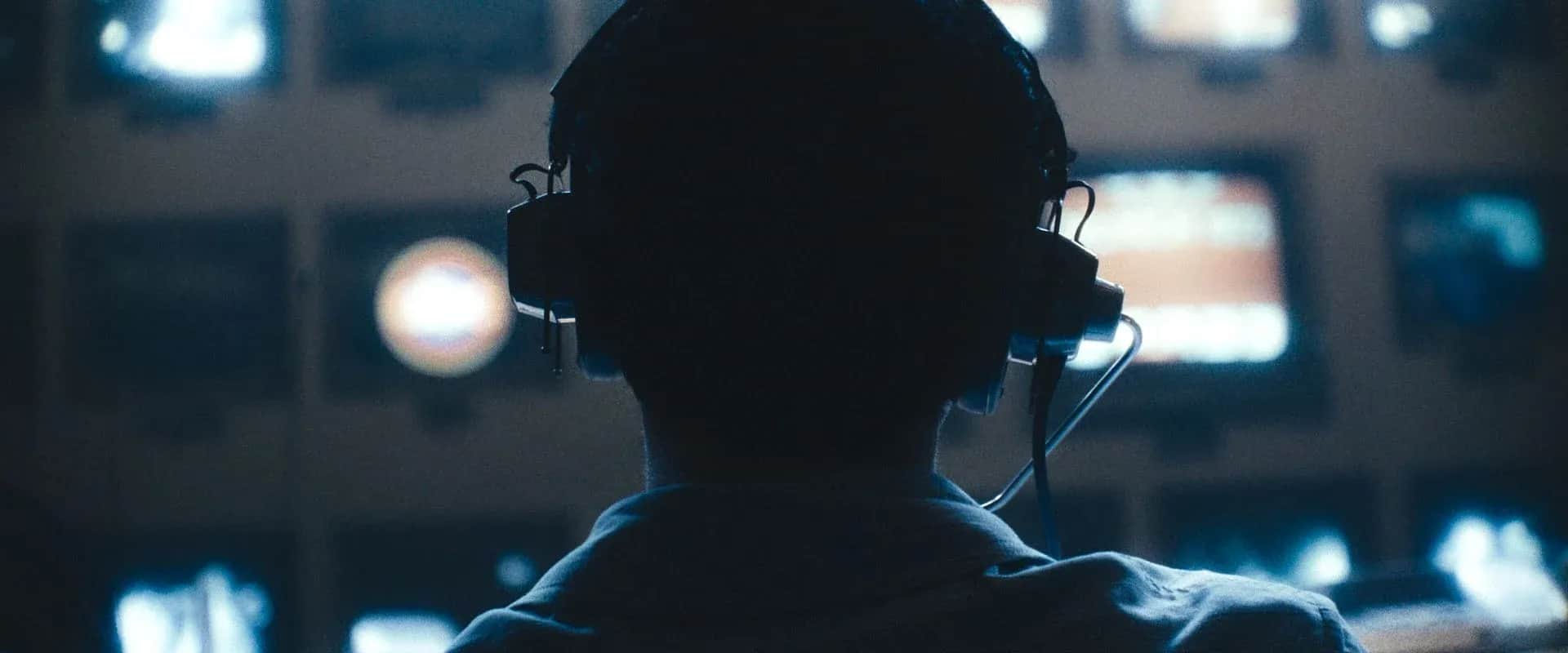 Personne vue de dos, portant un casque audio devant un mur d’écrans lumineux