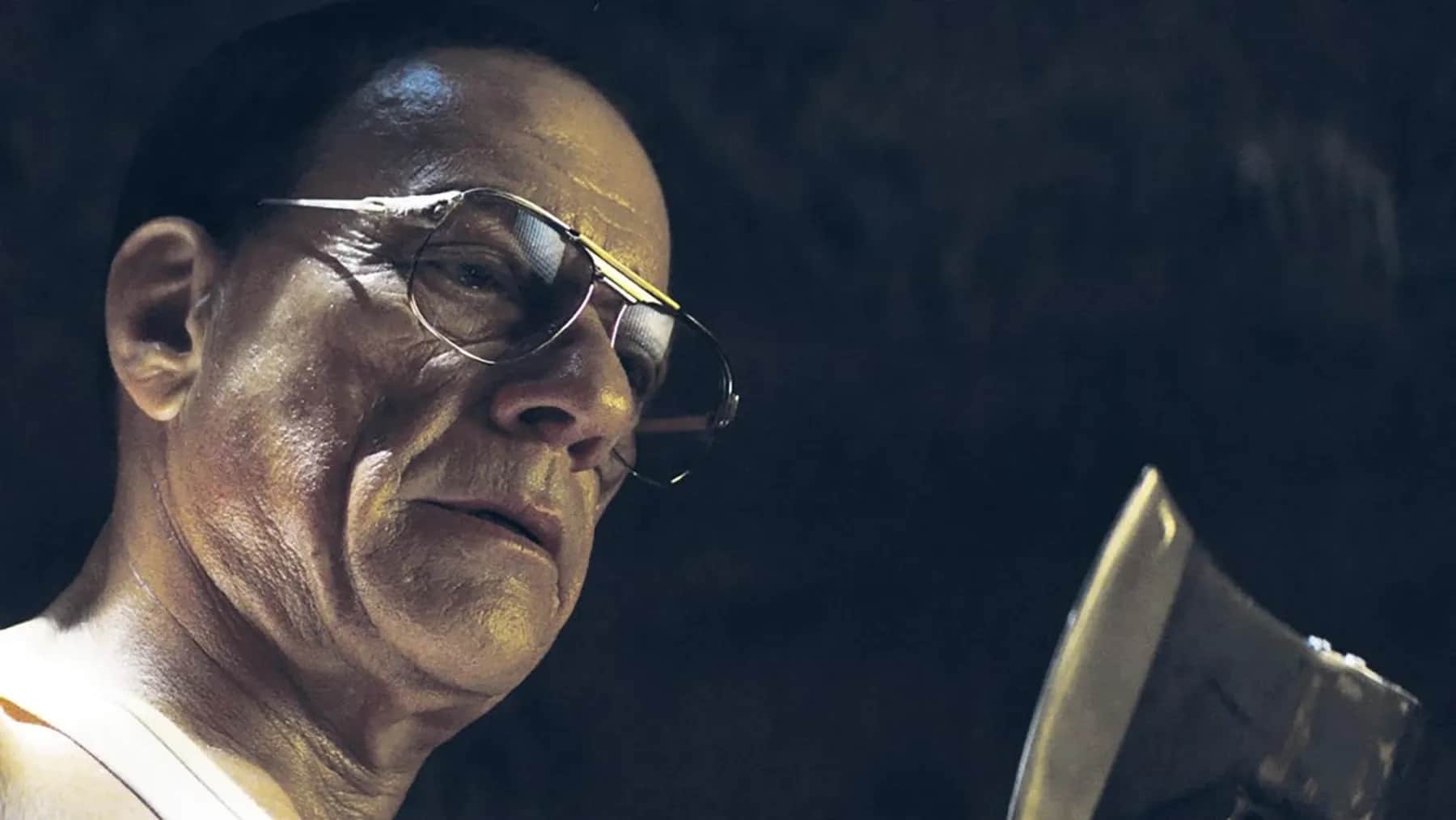 Un homme chauve portant des lunettes observe un objet métallique dans une ambiance sombre