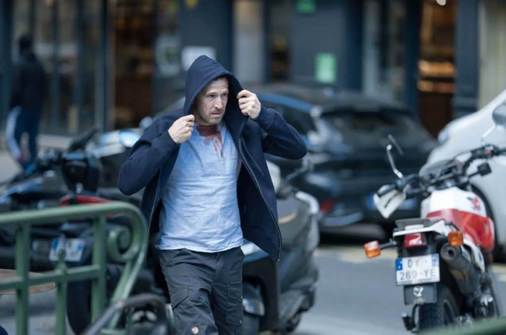 Homme en veste à capuche marchant dans une rue bordée de scooters et de voitures