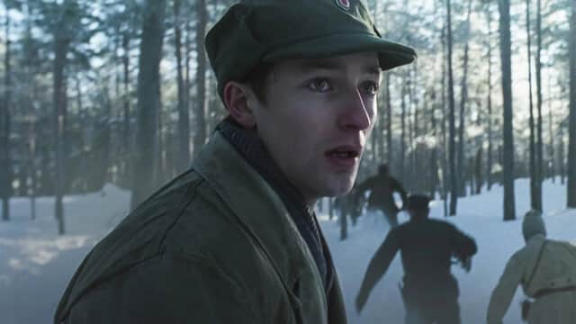 Un jeune homme en uniforme militaire dans une forêt enneigée, regardant en arrière tandis que d'autres courent.