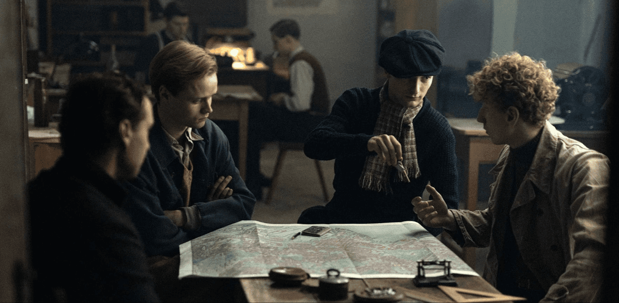 Quatre hommes réunis autour d’une carte dépliée dans un intérieur sombre.