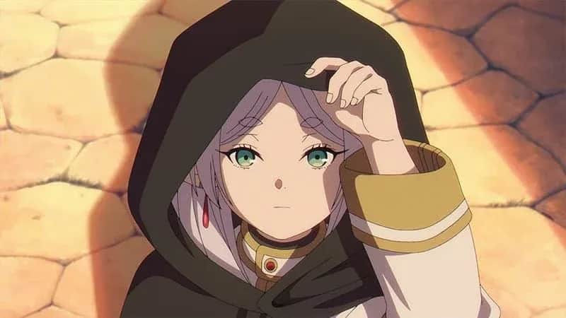 Jeune femme aux cheveux violets, portant une cape noire, levant une main vers sa capuche devant un mur de pierres.
