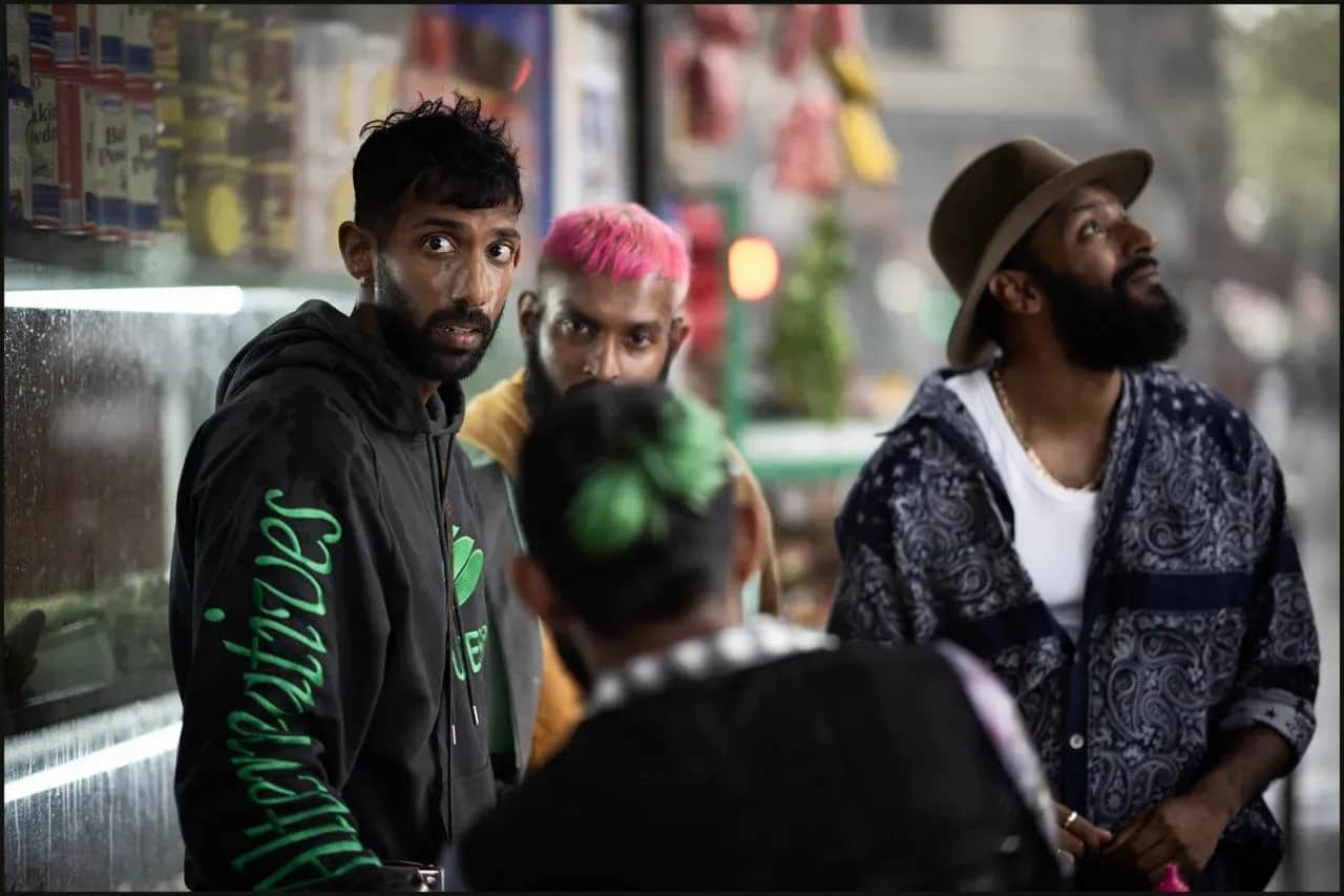 Un groupe de personnes dans une boutique, dont un homme barbu portant un chapeau et un homme aux cheveux roses.