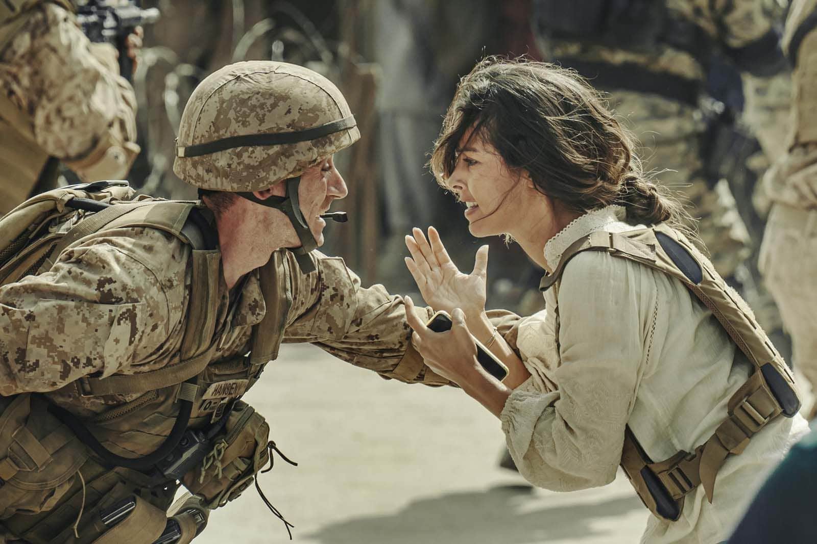 Un soldat casqué face à une femme, qui lui parle en levant la main, dans un décor militaire.