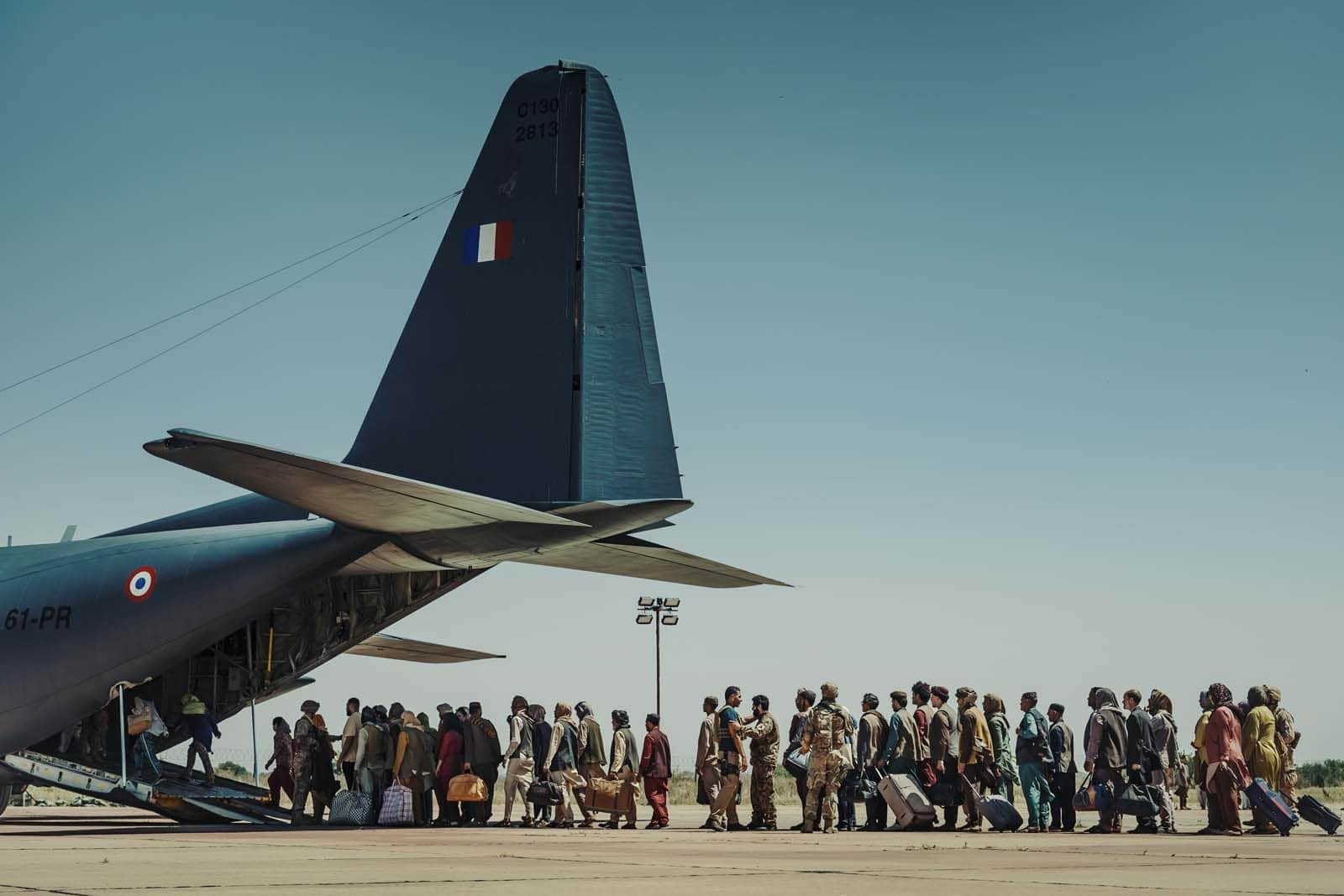 Un avion de transport militaire devant lequel un groupe de personnes avance avec des bagages sur un tarmac.