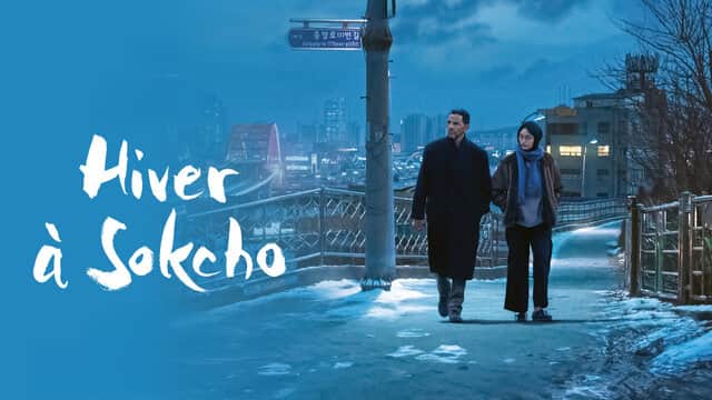Affiche de « Hiver à Sokcho » avec un homme et une femme marchant sur un pont enneigé la nuit.