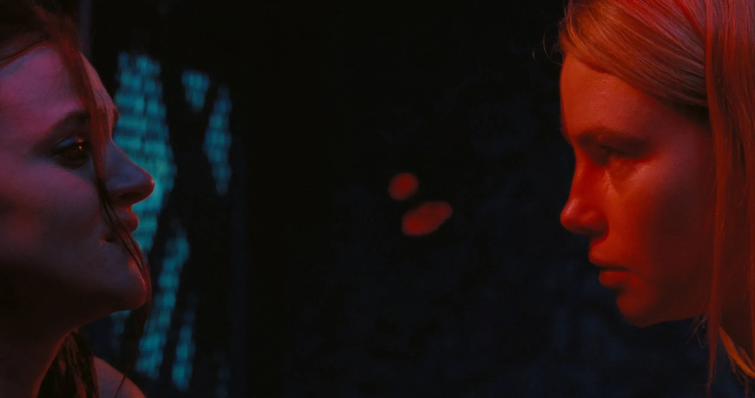 Deux femmes se font face en gros plan dans une lumière rouge et bleue.