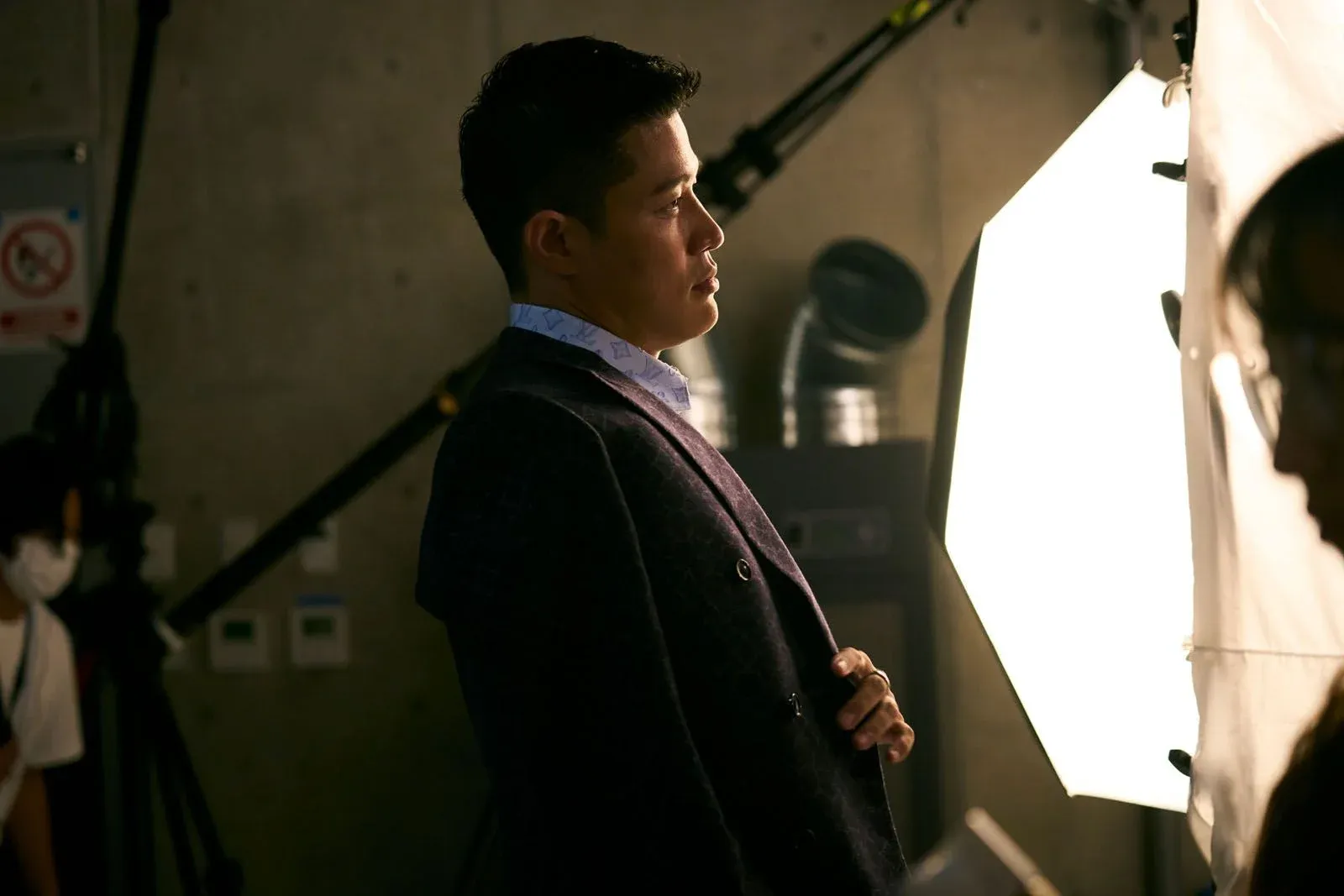 Homme en costume posant devant un grand projecteur dans un studio de tournage
