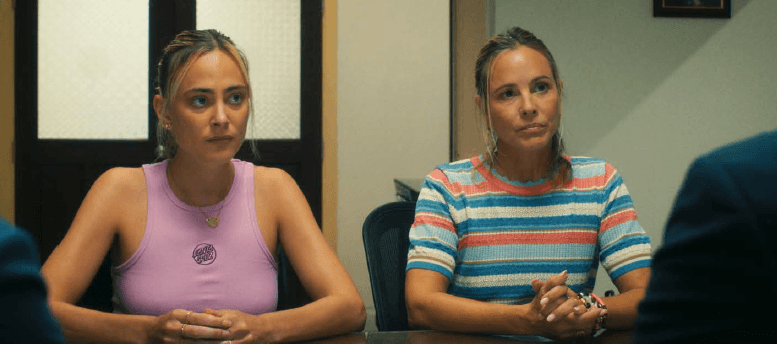 Deux femmes assises à une table, face à des interlocuteurs dans une pièce.