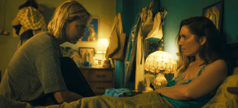 Deux femmes se font face dans une chambre, l’une assise sur un lit et l’autre penchée vers elle.